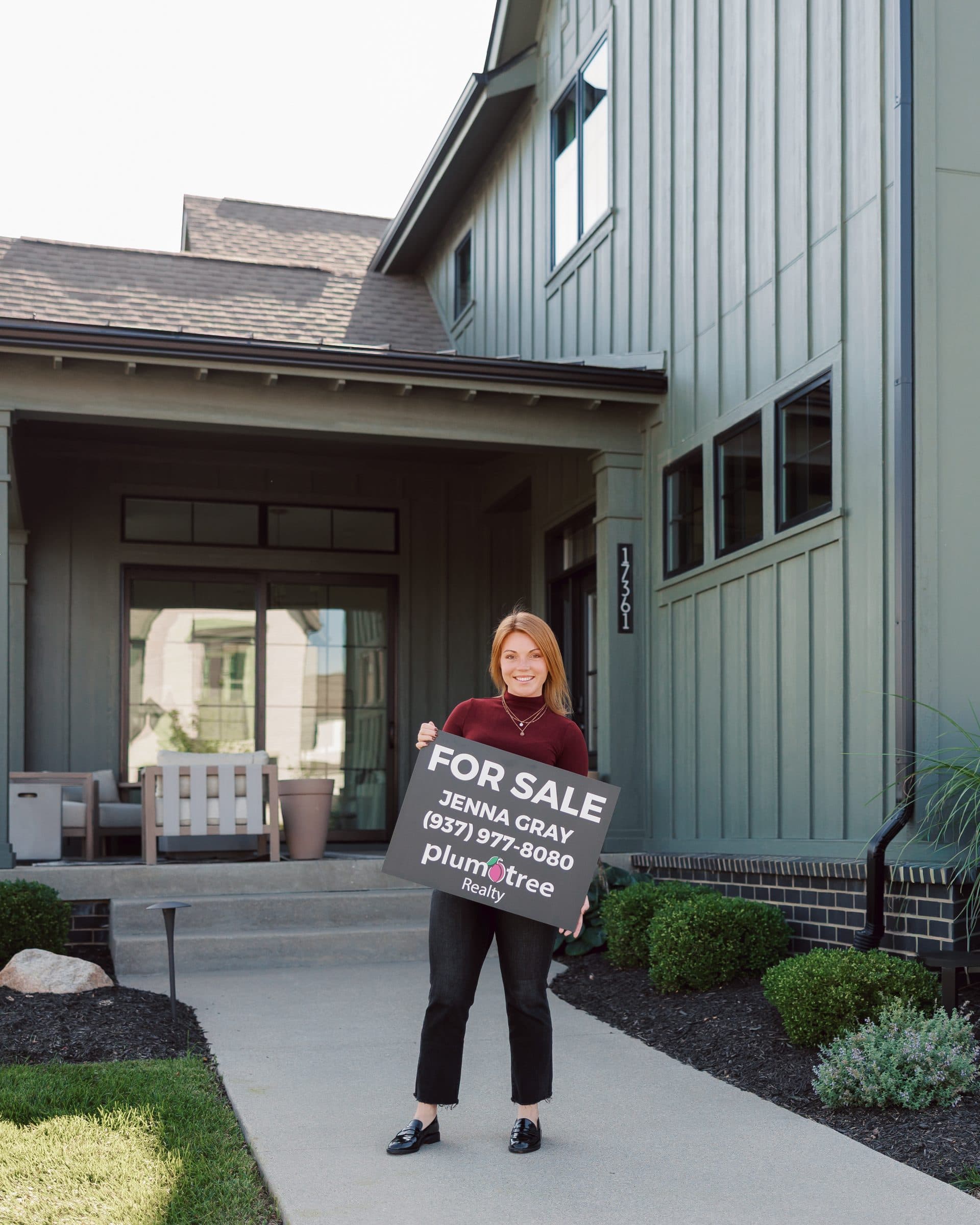 Jenna Gray, Dayton realtor, with a Plum Tree Realty for sale sign in front of a house in the Dayton area