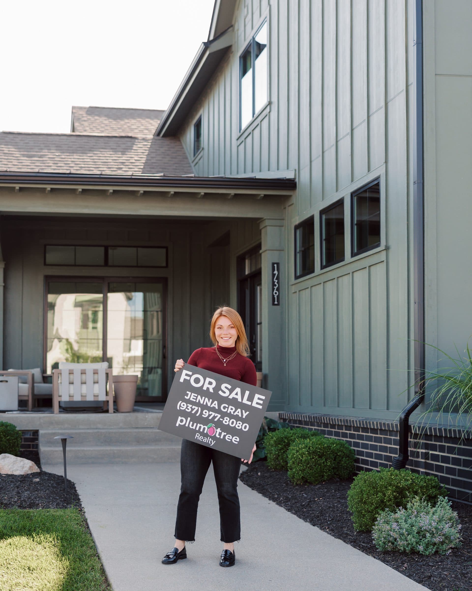 Jenna Gray, Dayton realtor, carrying a Plum Tree Realty for sale sign up a front path